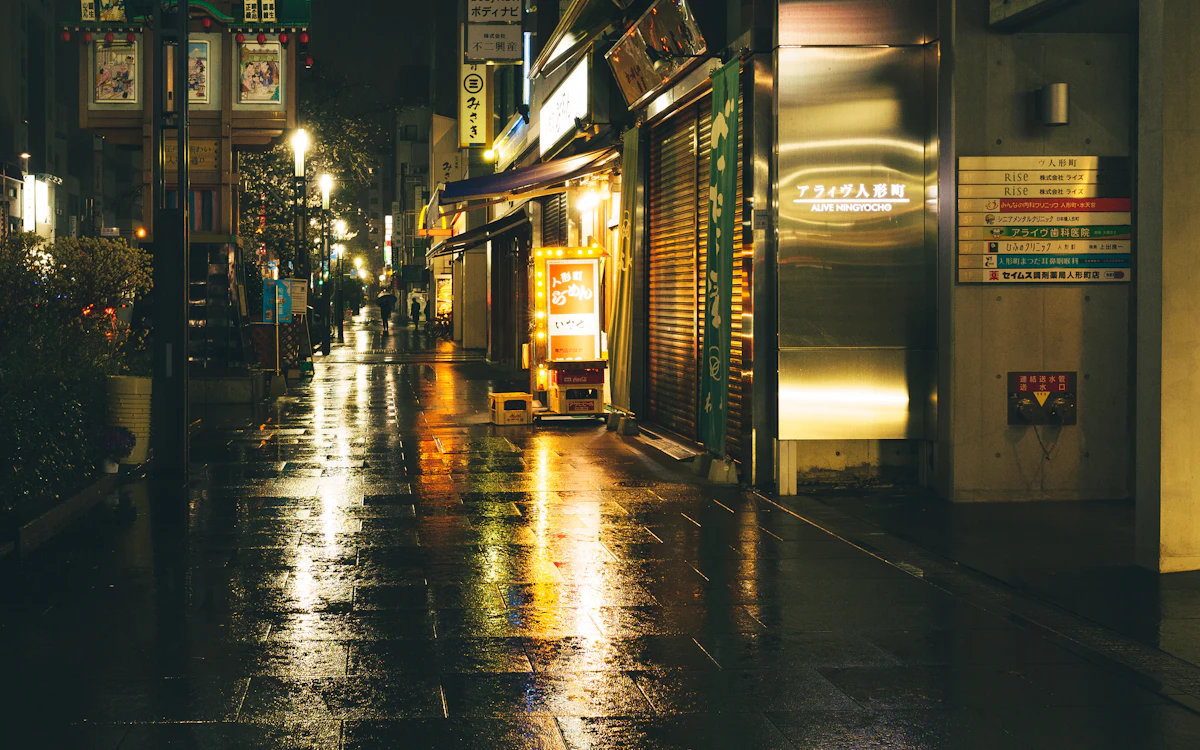 A rainy night street reflecting shop lights